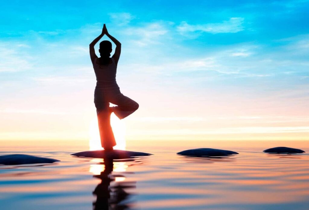 Person im Yoga-Stand bei Sonnenaufgang über dem Wasser – Symbol für Balance, mentale Klarheit und achtsames Leben.